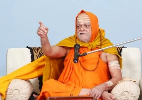 Nishchalananda Saraswati seated on a white sofa, gesturing emphatically as he explains a point into a microphone