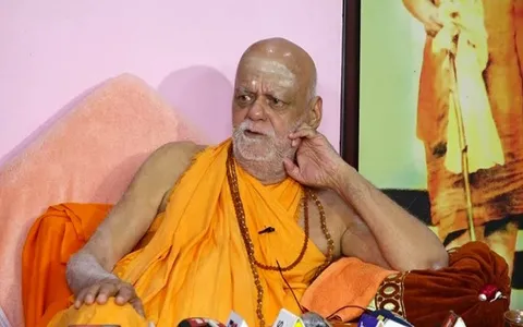 Nishchalananda Saraswati seated before a cluster of press microphones, resting his cheek on his hand as he listens