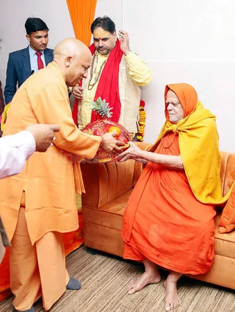 Nishchalananda Saraswati seated as visitors in saffron and white present a platter of fruit