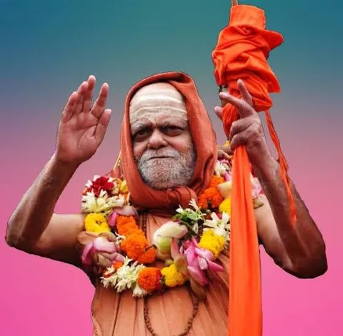 Nishchalananda Saraswati garlanded with marigolds, raising his hand in blessing while holding the monastic staff wrapped in saffron cloth